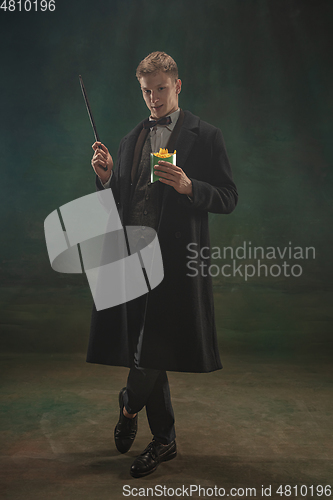 Image of Young man in art action isolated on dark green background. Retro style, comparison of eras concept.