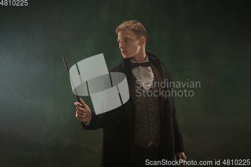 Image of Young man in art action isolated on dark green background. Retro style, comparison of eras concept.