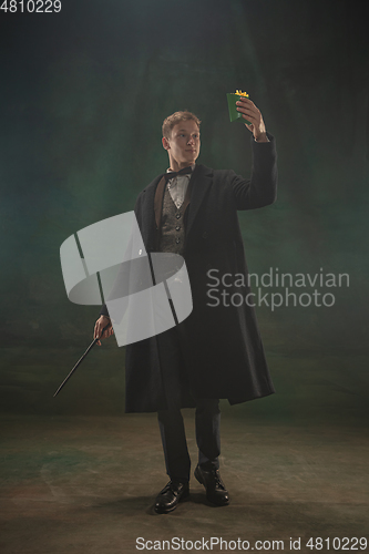 Image of Young man in art action isolated on dark green background. Retro style, comparison of eras concept.