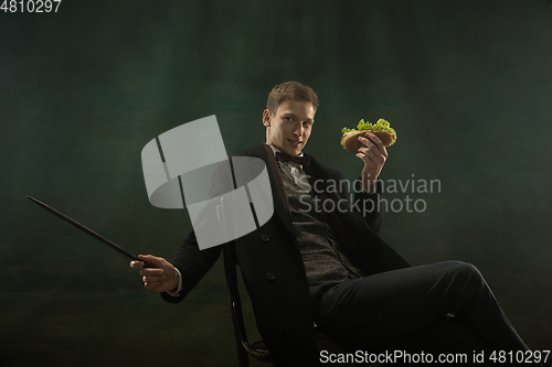 Image of Young man in art action isolated on dark green background. Retro style, comparison of eras concept.