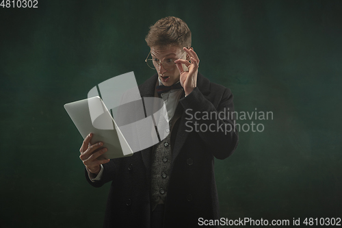 Image of Young man in art action isolated on dark green background. Retro style, comparison of eras concept.