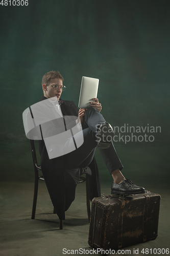 Image of Young man in art action isolated on dark green background. Retro style, comparison of eras concept.