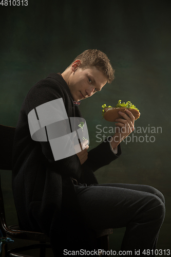 Image of Young man in art action isolated on dark green background. Retro style, comparison of eras concept.