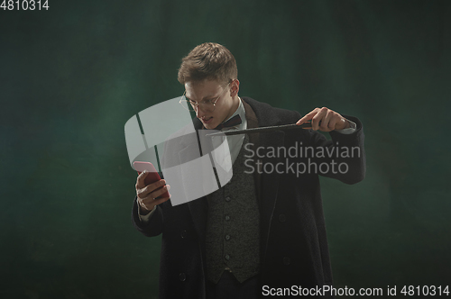 Image of Young man in art action isolated on dark green background. Retro style, comparison of eras concept.