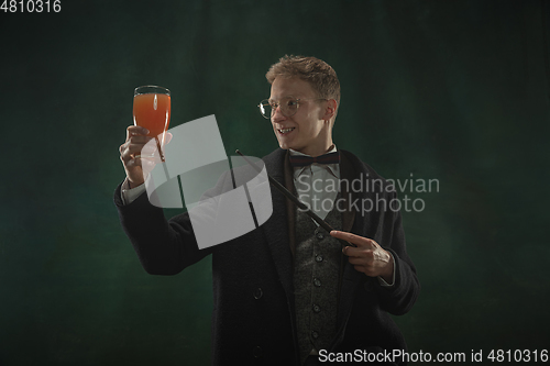 Image of Young man in art action isolated on dark green background. Retro style, comparison of eras concept.