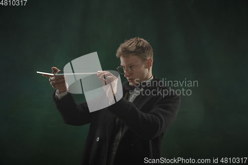 Image of Young man in art action isolated on dark green background. Retro style, comparison of eras concept.