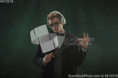 Image of Young man in art action isolated on dark green background. Retro style, comparison of eras concept.