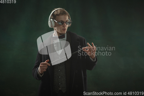 Image of Young man in art action isolated on dark green background. Retro style, comparison of eras concept.