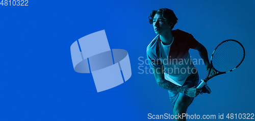 Image of Young caucasian man playing tennis isolated on blue studio background in neon, action and motion concept