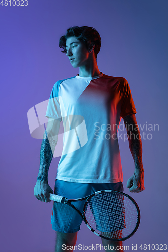 Image of Young caucasian man playing tennis isolated on purple-blue studio background in neon, action and motion concept
