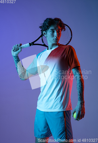 Image of Young caucasian man playing tennis isolated on purple-blue studio background in neon, action and motion concept