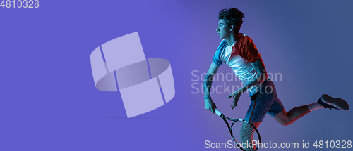 Image of Young caucasian man playing tennis isolated on purple-blue studio background in neon, action and motion concept