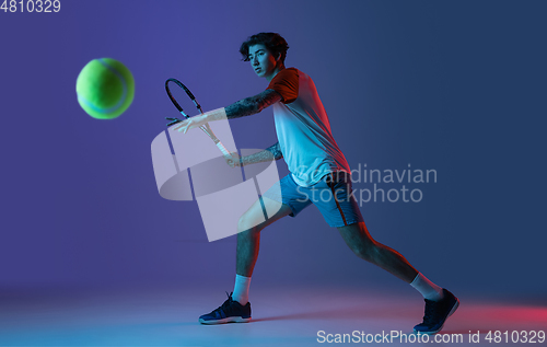 Image of Young caucasian man playing tennis isolated on purple-blue studio background in neon, action and motion concept