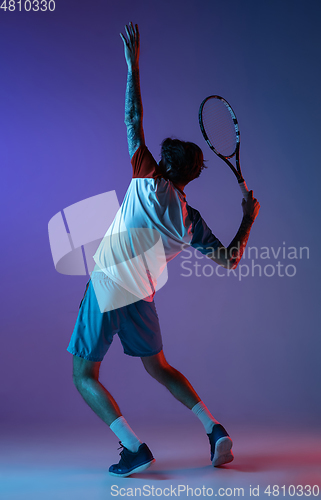 Image of Young caucasian man playing tennis isolated on purple-blue studio background in neon, action and motion concept