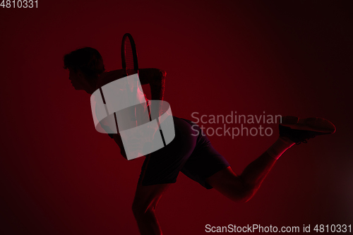 Image of Young caucasian man playing tennis isolated on red studio background in neon, action and motion concept