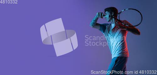 Image of Young caucasian man playing tennis isolated on purple-blue studio background in neon, action and motion concept