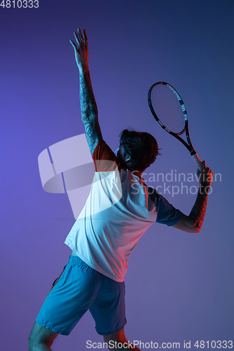 Image of Young caucasian man playing tennis isolated on purple-blue studio background in neon, action and motion concept