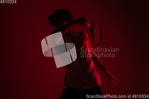 Image of Young caucasian man playing tennis isolated on red studio background in neon, action and motion concept