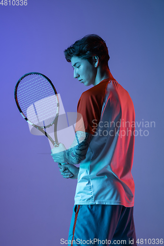 Image of Young caucasian man playing tennis isolated on purple-blue studio background in neon, action and motion concept