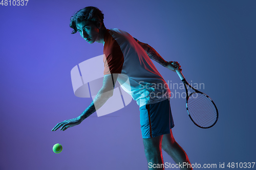 Image of Young caucasian man playing tennis isolated on purple-blue studio background in neon, action and motion concept
