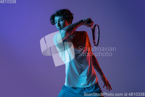 Image of Young caucasian man playing tennis isolated on purple-blue studio background in neon, action and motion concept