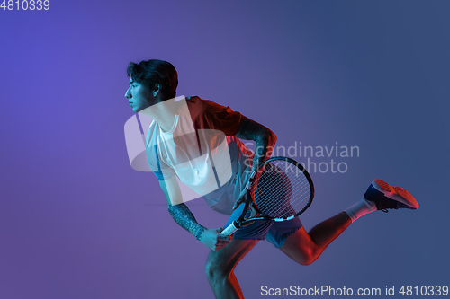 Image of Young caucasian man playing tennis isolated on purple-blue studio background in neon, action and motion concept