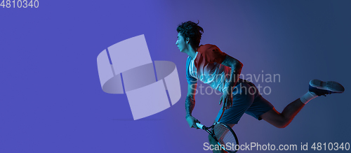 Image of Young caucasian man playing tennis isolated on purple-blue studio background in neon, action and motion concept