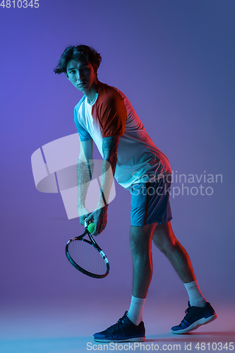 Image of Young caucasian man playing tennis isolated on purple-blue studio background in neon, action and motion concept