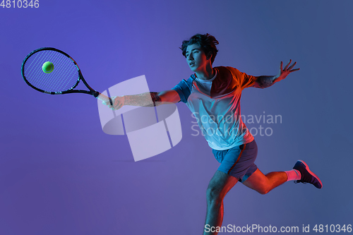 Image of Young caucasian man playing tennis isolated on purple-blue studio background in neon, action and motion concept