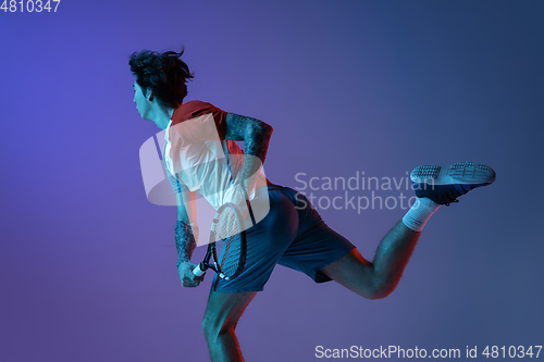 Image of Young caucasian man playing tennis isolated on purple-blue studio background in neon, action and motion concept