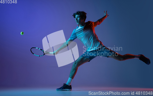 Image of Young caucasian man playing tennis isolated on purple-blue studio background in neon, action and motion concept