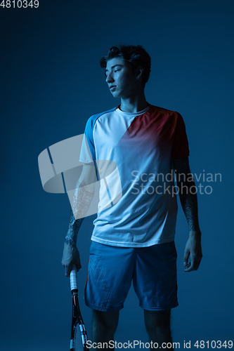 Image of Young caucasian man playing tennis isolated on blue studio background in neon, action and motion concept