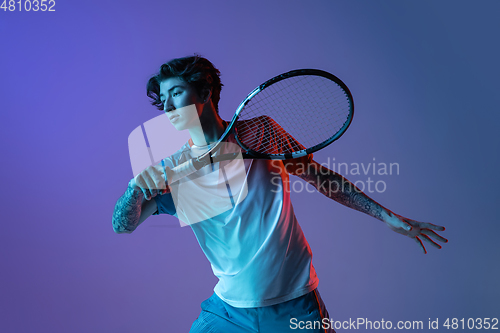 Image of Young caucasian man playing tennis isolated on purple-blue studio background in neon, action and motion concept