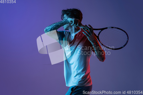 Image of Young caucasian man playing tennis isolated on purple-blue studio background in neon, action and motion concept