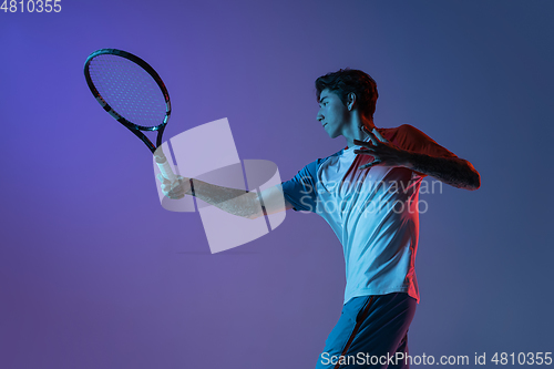Image of Young caucasian man playing tennis isolated on purple-blue studio background in neon, action and motion concept