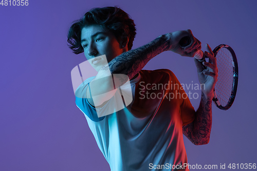 Image of Young caucasian man playing tennis isolated on purple-blue studio background in neon, action and motion concept
