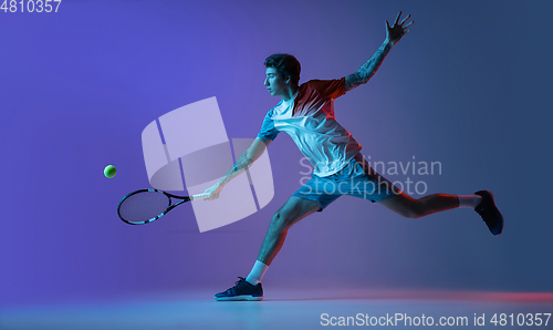 Image of Young caucasian man playing tennis isolated on purple-blue studio background in neon, action and motion concept