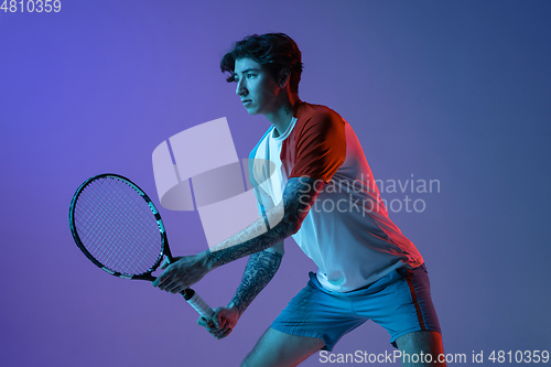 Image of Young caucasian man playing tennis isolated on purple-blue studio background in neon, action and motion concept