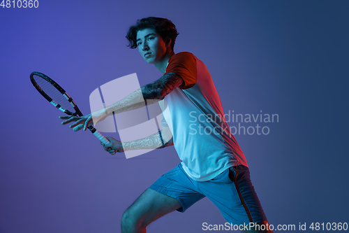 Image of Young caucasian man playing tennis isolated on purple-blue studio background in neon, action and motion concept