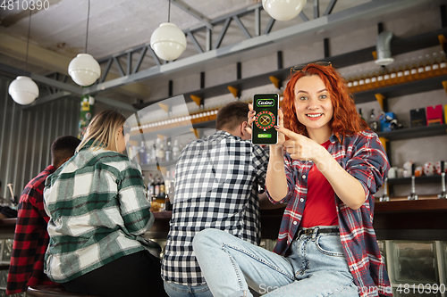 Image of Woman showing phone with betting app on screen. Emotional fans cheering for favourite team, watching on exciting game. Concept of friendship, leisure activity, emotions