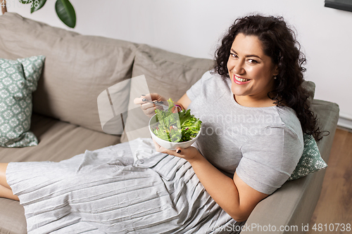 Image of smiling young woman eating vegetable salad at home