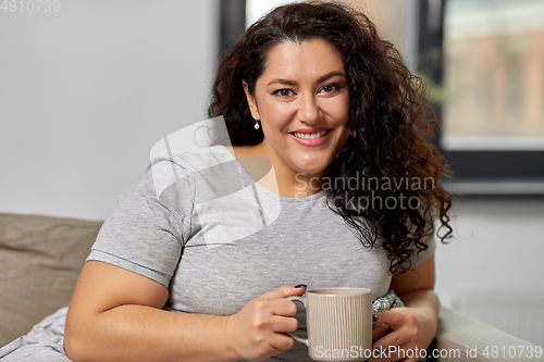 Image of happy woman drinking coffee or tea on sofa at home