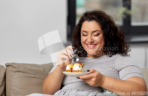 Image of smiling young woman eating cake at home