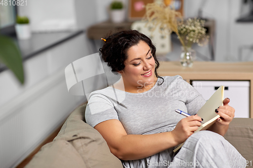 Image of happy young woman with diary on sofa at home