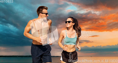 Image of couple in sports clothes running along on beach