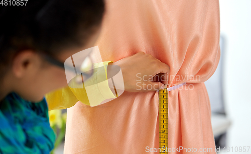 Image of fashion designer measuring dress with tape measure