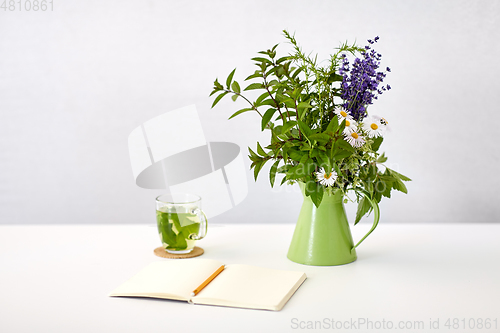 Image of herbal tea, notebook and flowers in jug on table