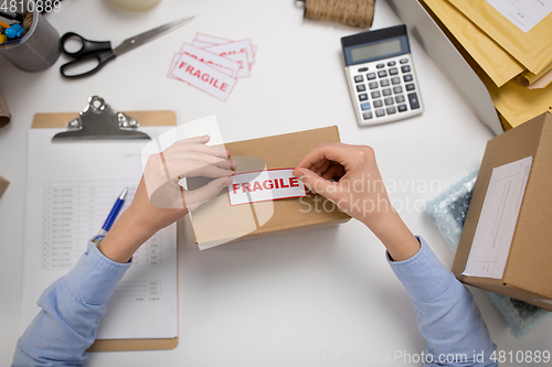 Image of woman sticking fragile mark to parcel box