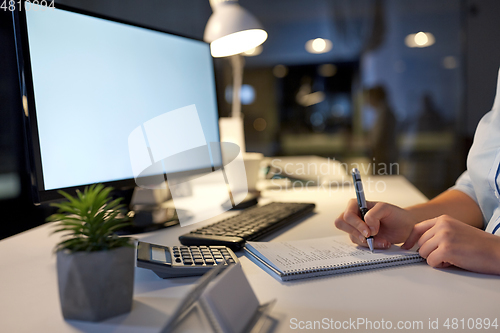 Image of businesswoman writing to notebook at night office