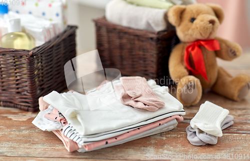 Image of baby clothes and teddy bear toy on table at home
